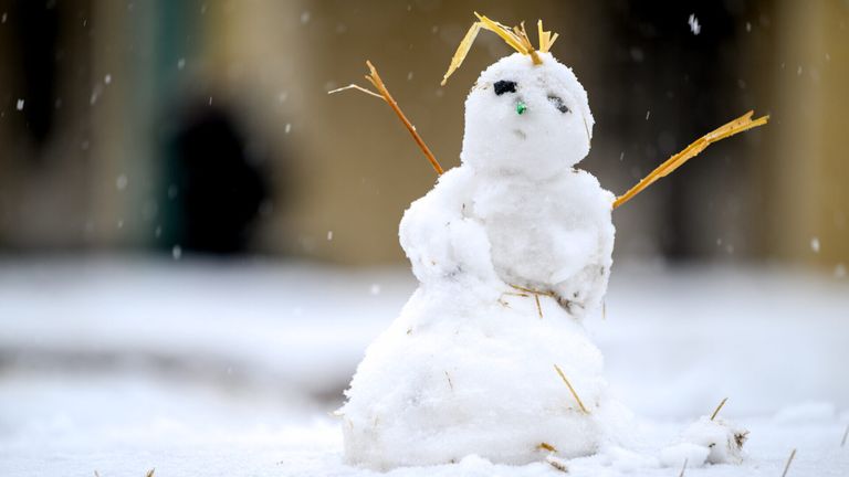Ein kleiner Schneemann mit grüner Nase und Stroharmen steht im Schnee, mit einem unscharfen Hintergrund.