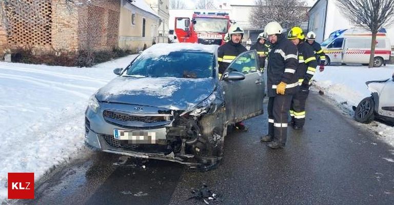 Ein beschädigtes Auto mit Feuerwehrleuten und einem Feuerwehrwagen in der Nähe. Die Front des Autos ist stark beschädigt, und Schnee bedeckt das Auto und den Boden.