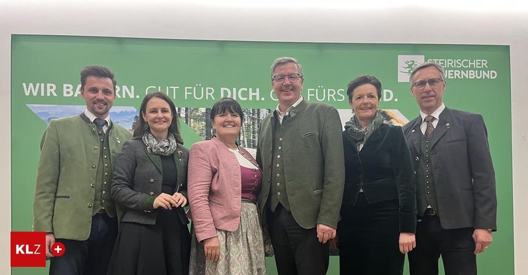 Fünf Personen, drei Frauen und zwei Männer, stehen zusammen vor einem grünen Banner. Sie lächeln und sind in traditioneller Kleidung gekleidet.