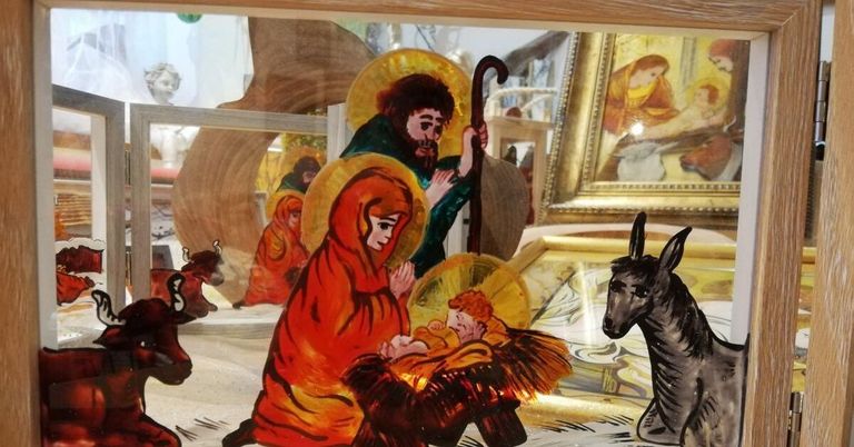 Ein Glasbild zeigt die Weihnachtsszene mit Maria, Josef und dem Jesuskind, zusammen mit anderen Figuren und einem Esel in einer Vitrine.