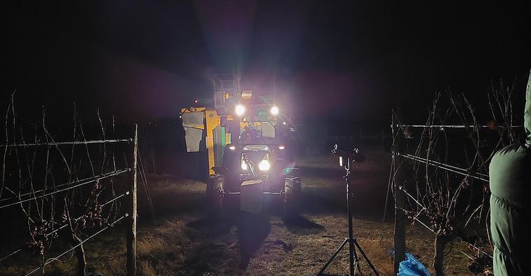 Ein Traktor mit eingeschalteten Scheinwerfern, nachts auf einem Feld geparkt. Ein Kamerastativ steht davor.