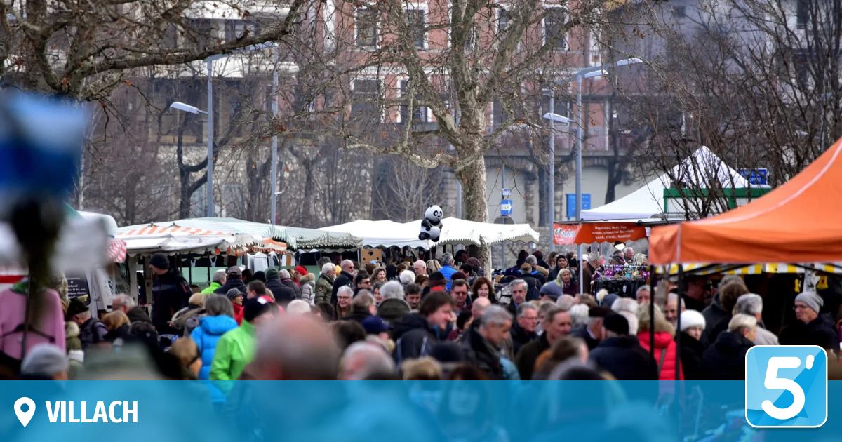 Eine Menschenmenge versammelt sich um Marktstände mit einem Panda-Ballon darüber. Straßenlaternen und Zelte sind vorhanden, und Gebäude sind im Hintergrund.