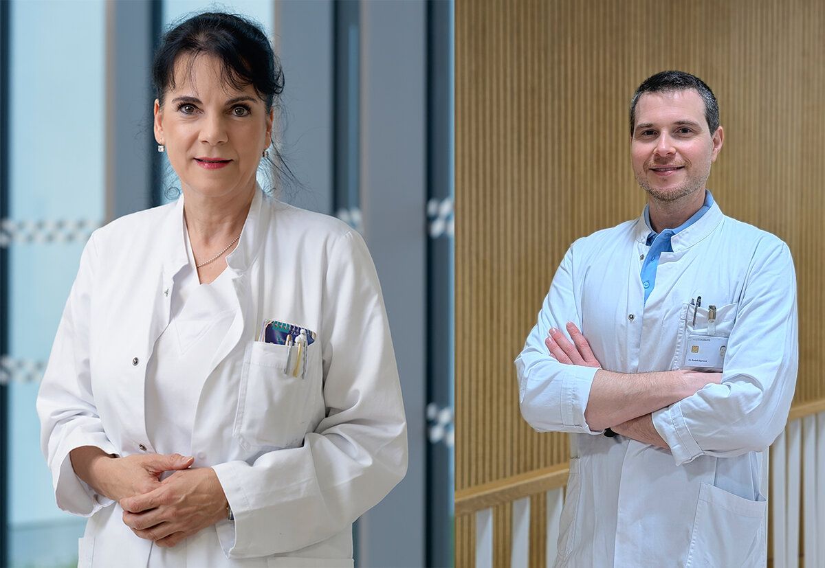 Zwei Ärzte in weißen Kitteln, eine Frau und ein Mann, stehen nebeneinander. Die Frau hat eine Halskette und Ohrringe und einen Stift in der Tasche. Der Mann hat die Arme verschränkt.