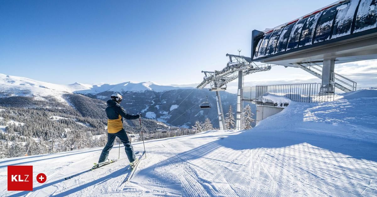 Ein Skifahrer steht auf einer verschneiten Piste, nahe einer Skilift und einem verschneiten Berg im Hintergrund.