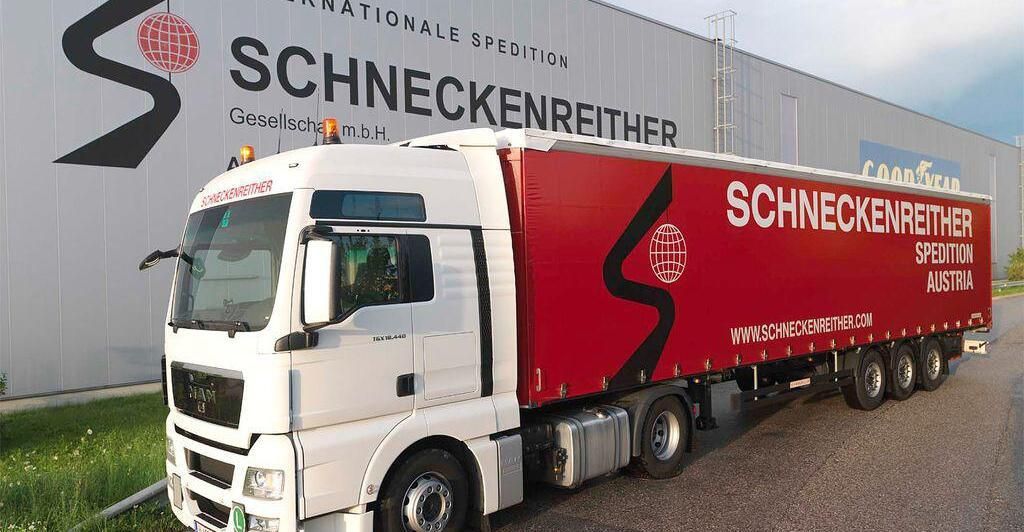 Ein weißer und roter LKW mit dem Wort Schneckenreither an der Seite ist vor einem Gebäude geparkt.
