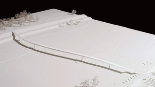 Ein weißes Landschaftsmodell zeigt eine Brücke auf einem verschneiten Gelände mit spärlichen Bäumen und Schatten.