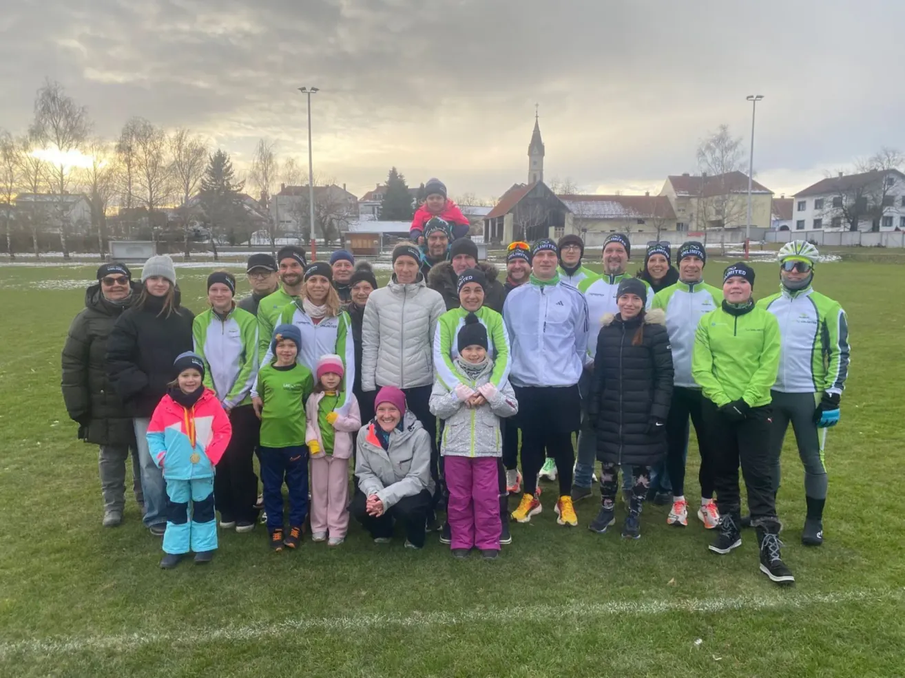 Eine Gruppe von Menschen in passenden Jacken posiert für ein Foto auf einem Feld, mit einem bewölkten Himmel im Hintergrund.