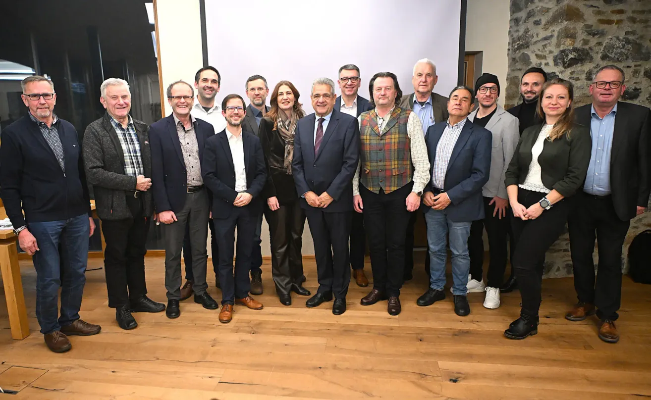 Eine Gruppe von Menschen in formeller Kleidung steht lächelnd zusammen und posiert für ein Foto auf einem Holzboden.