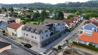 Luftaufnahme eines modernen Gebäudes mit mehreren Fenstern und einem Balkon, umgeben von Wohnhäusern und Grünflächen.