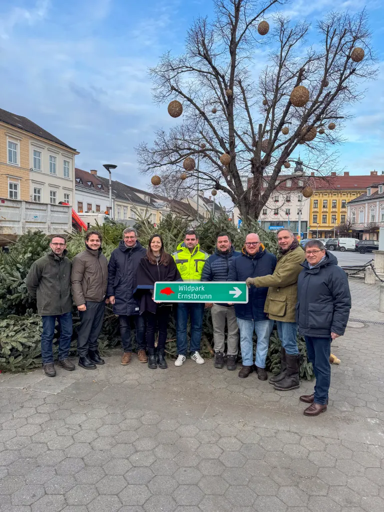 Eine Gruppe von Menschen posiert mit einem Schild für Ernstbrunn vor einem Baum und Tannen.