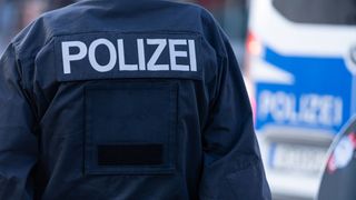 Der Rücken eines dunkelblauen Polizeiuniforms mit dem Wort 'POLIZEI' auf der Schulter aufgedruckt.