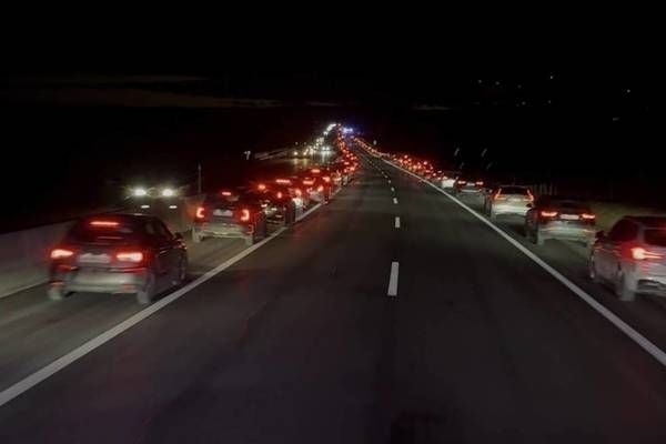Ein nächtlicher Blick auf eine Autobahn zeigt eine lange Reihe von Autos, deren Rückleuchten rot leuchten. Die Straße hat weiße Fahrspurmarkierungen.