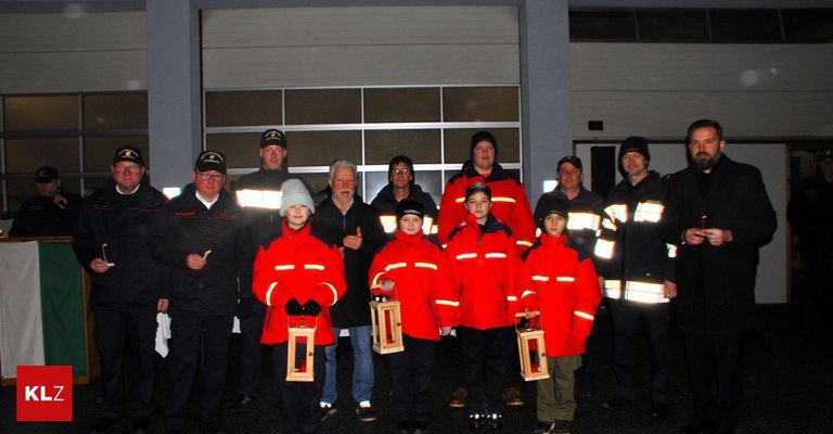 Eine Gruppe von Feuerwehrleuten und Kindern in roten Jacken und Mützen steht draußen, hält Laternen und posiert für ein Foto.