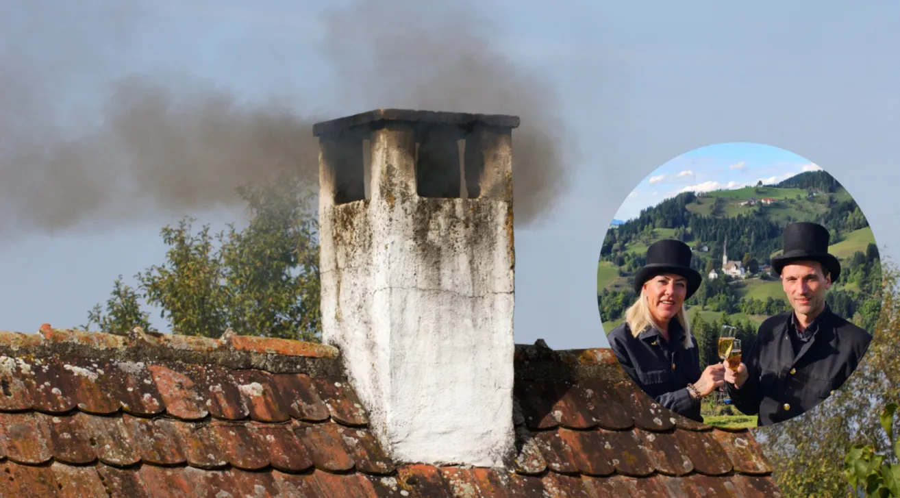 Ein Schornstein mit Rauch, der aus ihm austritt, wird vor dem Hintergrund einer Frau in einem schwarzen Hut gezeigt. Der Schornstein befindet sich auf einem Dach. Bäume und Berge sind im Hintergrund zu sehen.