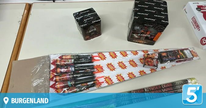 Auf einem Tisch sind verschiedene Feuerwerke zu sehen, darunter eine Schachtel mit der Aufschrift Gladiator, eine weitere Schachtel und ein in Plastik verpacktes Bündel von Feuerwerkskörpern. Rechts ist teilweise eine weiße Schachtel zu sehen.