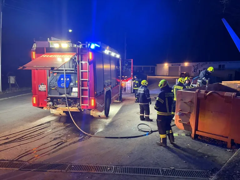 Feuerwehrleute versammeln sich bei Nacht um einen roten Feuerwehrwagen, dessen Lichter eingeschaltet sind, und sie bereiten sich auf einen Notfall vor.