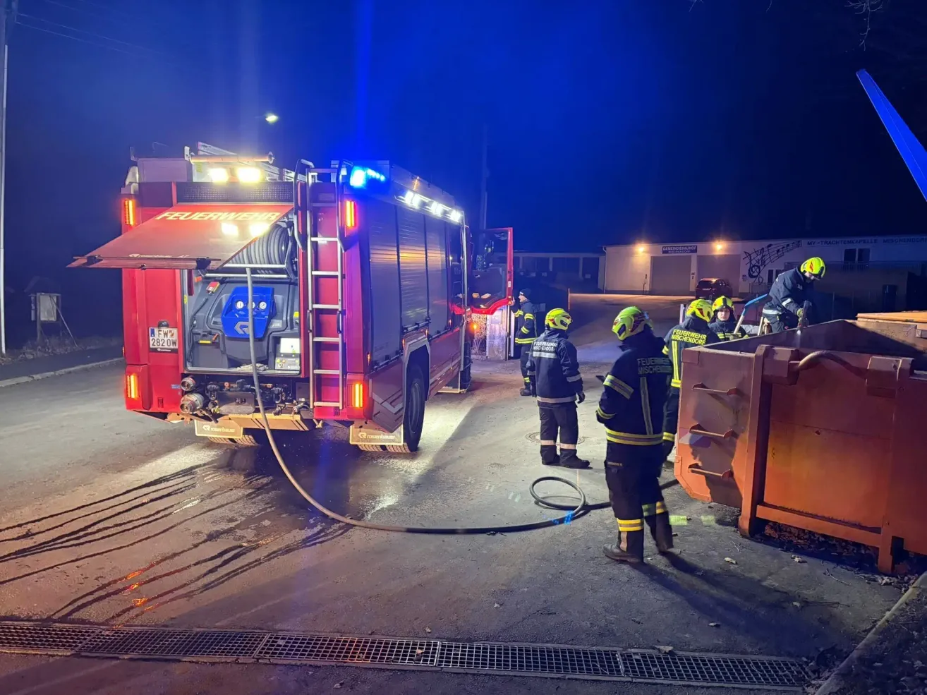 Feuerwehrleute versammeln sich bei Nacht um einen roten Feuerwehrwagen, dessen Lichter eingeschaltet sind, und sie bereiten sich auf einen Notfall vor.