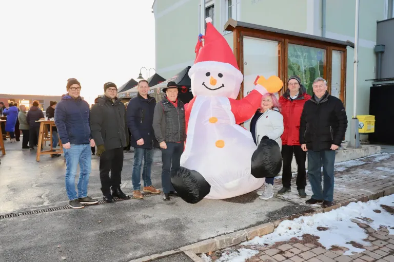Eine Gruppe von Menschen steht neben einem riesigen aufblasbaren Schneemann vor einem Gebäude im Winter.