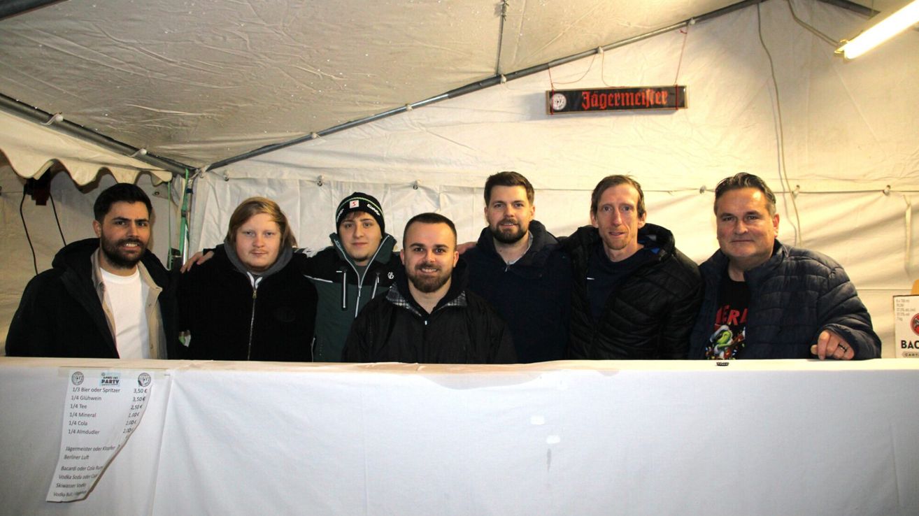 Eine Gruppe von Männern in Winterkleidung posiert für ein Foto in einem weißen Zelt mit einem Schild, auf dem Jagermeister steht.