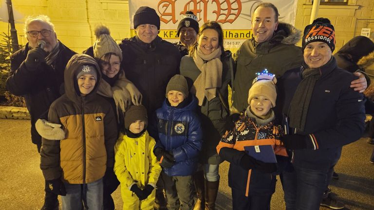 Eine Familie von acht Personen steht in Winterkleidung zusammen. Sie lächeln und scheinen für ein Foto zu posieren. Die Kinder sind mit Mützen und Handschuhen eingepackt.