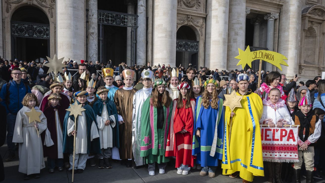 Eine Gruppe von Kindern in verschiedenen farbenfrohen Kostümen, einschließlich Kronen, posiert für ein Foto vor einem großen Gebäude.