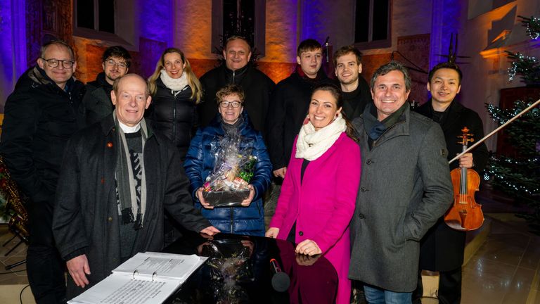 A group of people are posing for a photo with a gift basket in front of a piano.
