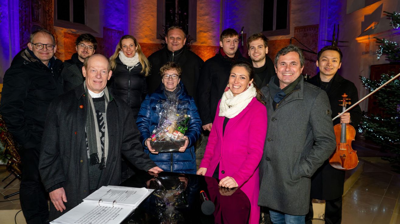 A group of people are posing for a photo with a gift basket in front of a piano.