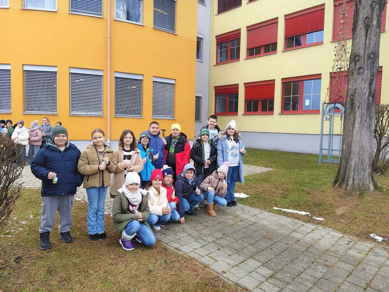 Eine Gruppe von Kindern und Jugendlichen posiert für ein Foto vor einem gelben Gebäude mit roten Fensterläden.