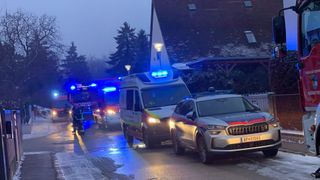 Emergency vehicles are parked on the side of the road with lights on. A police car is nearby. The sky is cloudy.