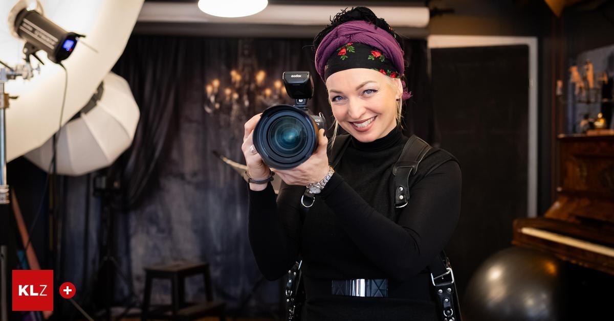 A woman wearing a black shirt and a purple headband is smiling while holding a camera with a flash on top.