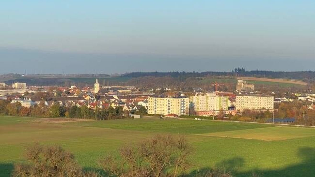 A panoramic view of a town with many buildings, a tower, and green fields. The sky is clear.