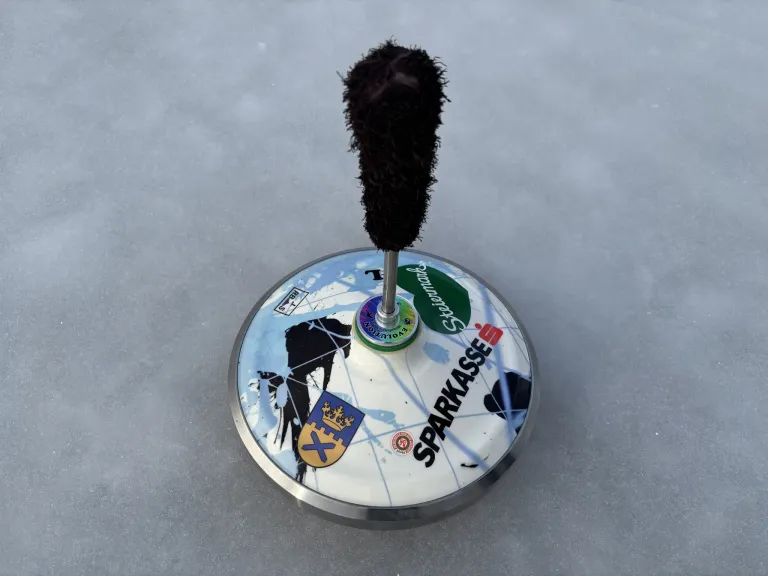 Ein metallischer Drehteller mit verschiedenen Aufklebern und einer schwarzen Bürste auf Eis, beschriftet mit 'SPARKASSE' und zusätzlichen Logos und Text.