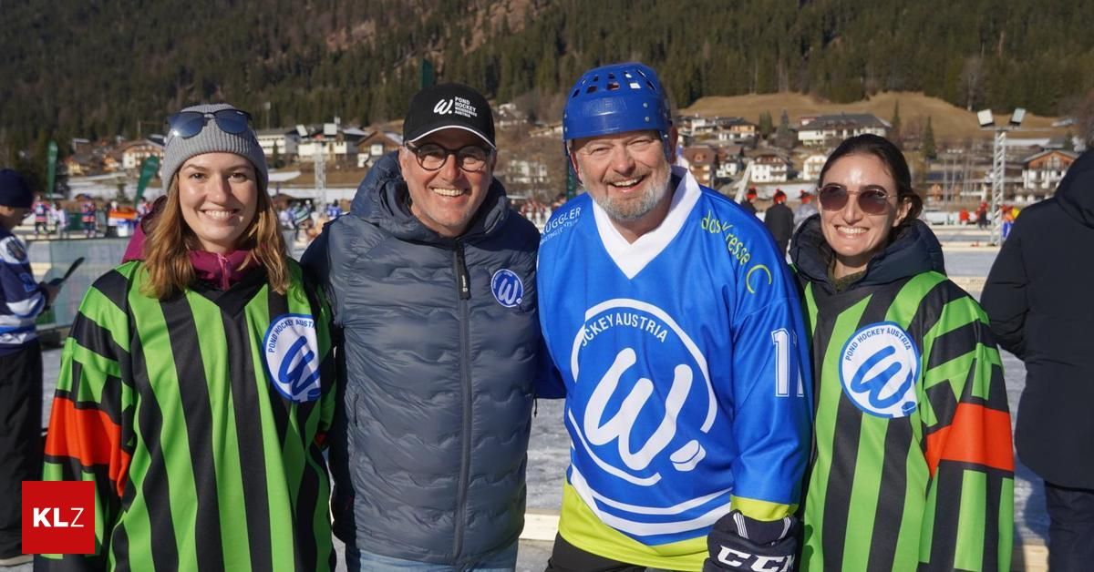 Four people are posing for a photo on a snowy field, with mountains in the background. They are all smiling and wearing winter clothes and helmets.