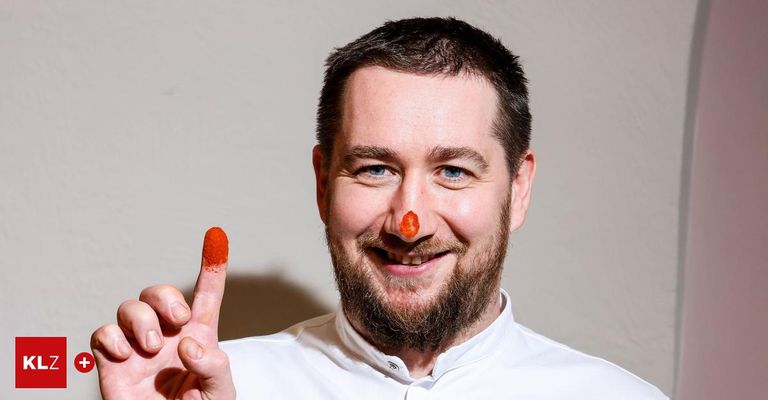 A chef with a red substance on his nose and finger, smiling for a photo, wearing a white shirt.