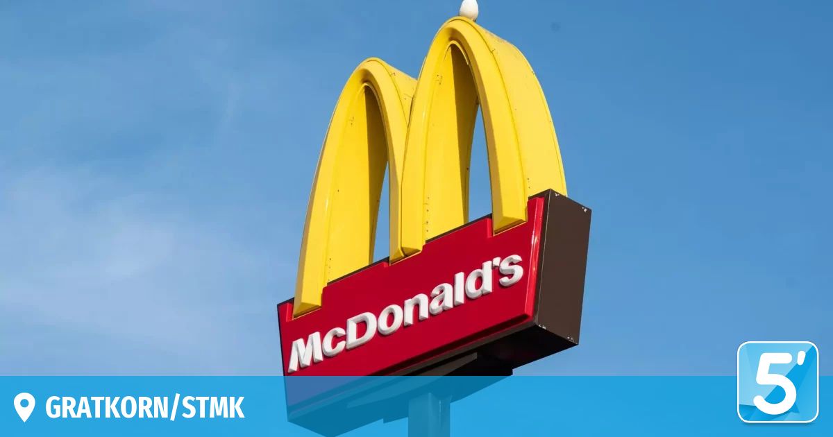 A yellow and red McDonald's sign with iconic arches and the name in white, displayed against a blue sky. The sign is attached to a pole.