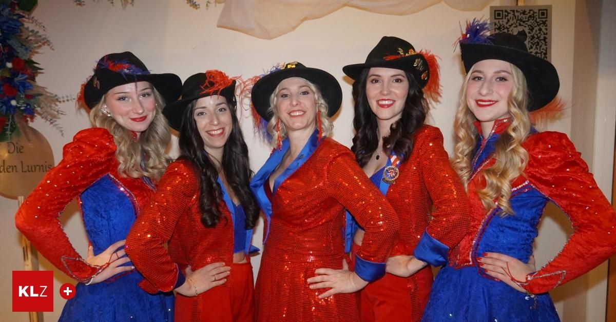 Fünf Frauen in roten Paillettenkleidern und schwarzen Hüten mit Federn stehen eng beieinander und lächeln für ein Foto. Jede Frau trägt roten Lippenstift.