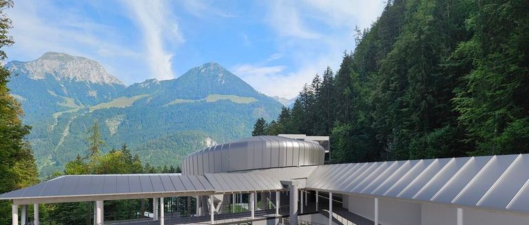 Ein modernes Gebäude mit gewölbtem Dach, gelegen in einem bewaldeten Gebiet mit Bergen im Hintergrund.