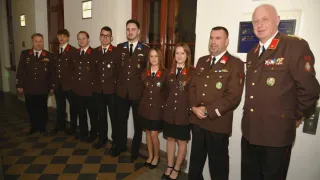 Eine Gruppe uniformierter Personen, einschließlich Männer und Frauen, steht in einer Reihe und lächelt für die Kamera. Sie tragen Medaillen und einige haben Schärpen.