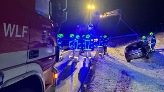 A group of firefighters in blue uniforms are standing on a snowy road at night. A fire truck is parked nearby.