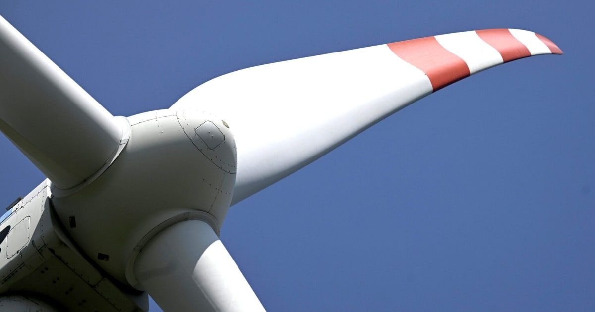 A close-up of a wind turbine blade with red and white stripes on a clear blue sky background.