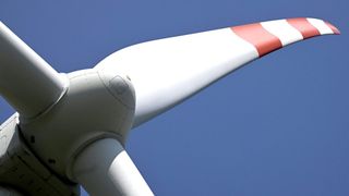 A close-up of a wind turbine blade with red and white stripes on a clear blue sky background.