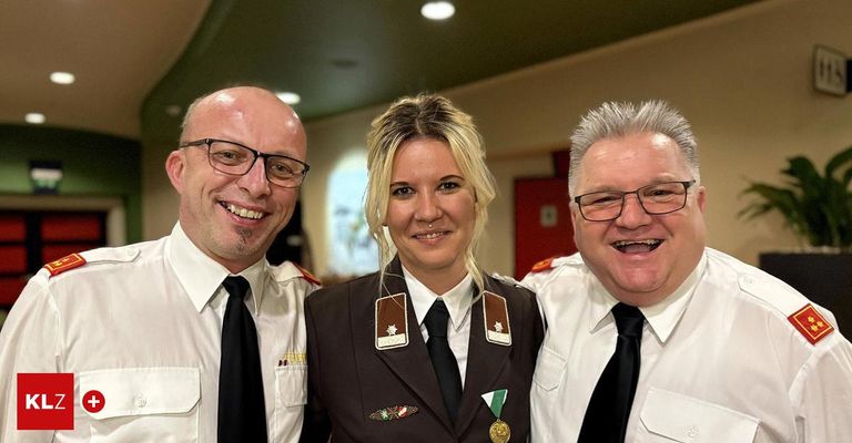 Three uniformed individuals, two men and one woman, are smiling for a photo. They all wear black ties and white shirts. The woman has a badge and a medal. Behind them, a red door is visible.
