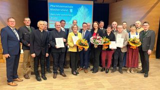 A group of people dressed in formal attire pose for a photo with certificates and flowers, possibly at a New Year's reception.