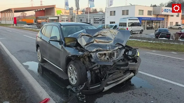 A severely damaged BMW SUV with a crushed front is parked on the side of the road, with a white van parked behind it.