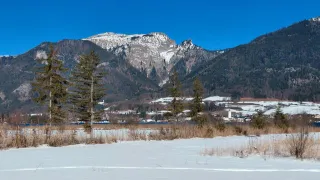 A snowy landscape with mountains in the background, trees and a river in the foreground.