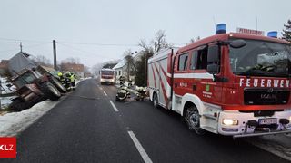 Firefighters are attending to an incident on a road. A fire truck is parked with its emergency lights on. Workers are repairing the road.