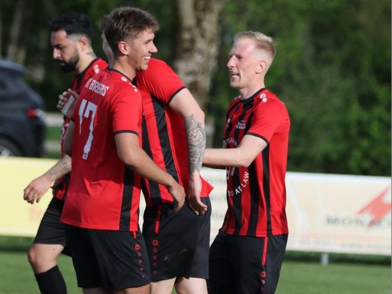 Vier Fußballspieler in roten Trikots feiern auf dem Spielfeld, einer trägt ein Trikot mit der Nummer 17.