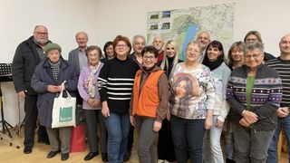 A group of adults in a room, standing in front of a map on the wall, smiling and posing for a photograph.