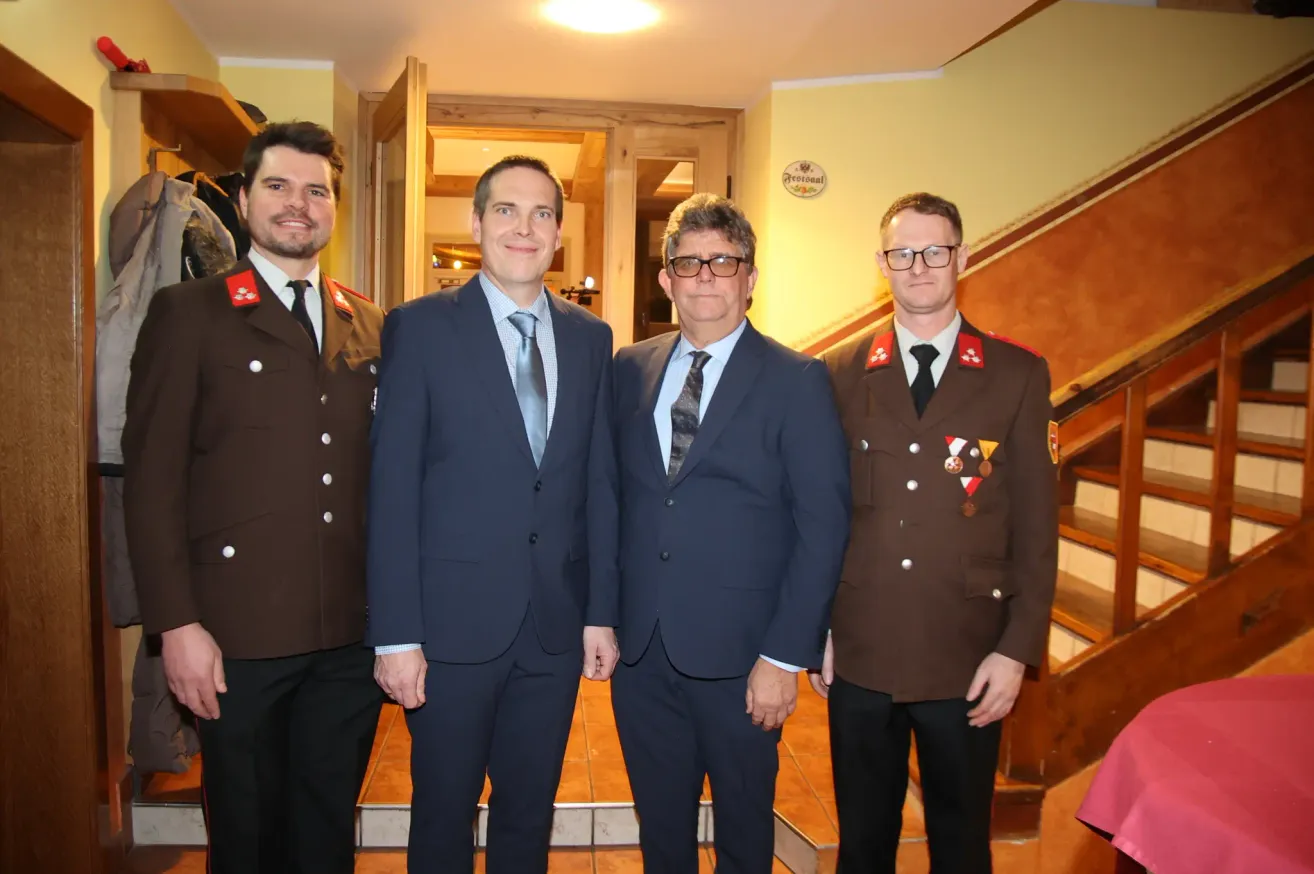Four men in suits and ties, two in military uniforms, pose for a photo indoors.