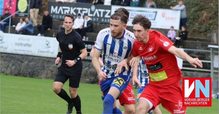 Drei Fußballspieler auf einem Spielfeld. Ein Schiedsrichter in Schwarz hinter ihnen. Ein Spieler in Rot und ein anderer in blau-weißen Trikots. Sie sind in ein Wettkampfspiel verwickelt.